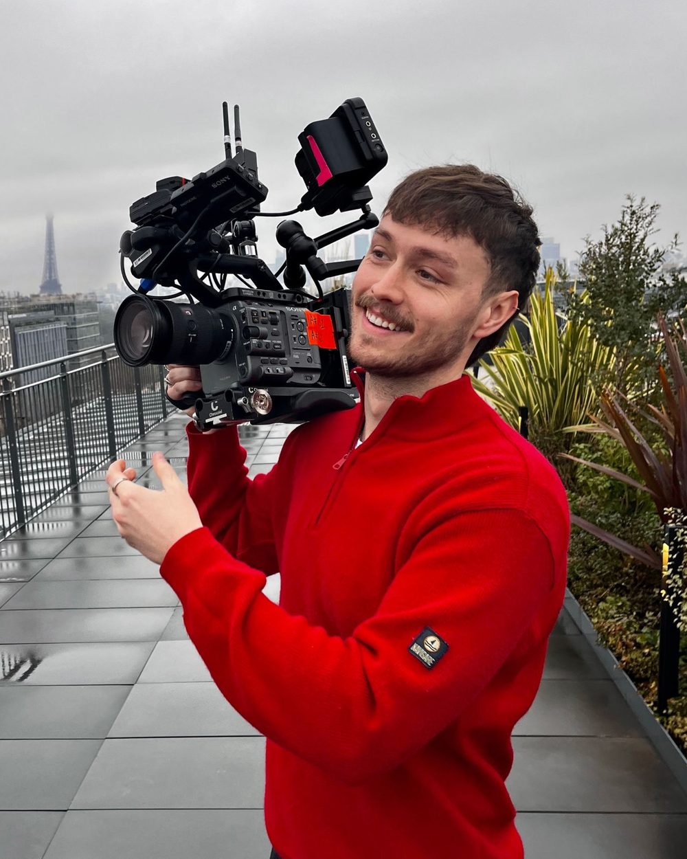Oliver Durnford on a rooftop shoot, smiling, with a camera on his shoulder