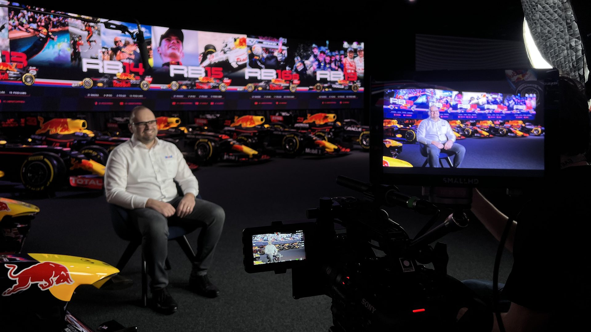 Behind the scenes at MK-7: a spokesperson lit in front of historic Red Bull Racing cars, with the A-camera and monitor in the foreground